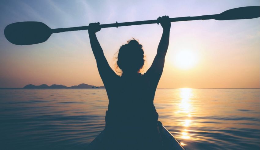 A woman is paddling a kayak in the ocean at sunset.