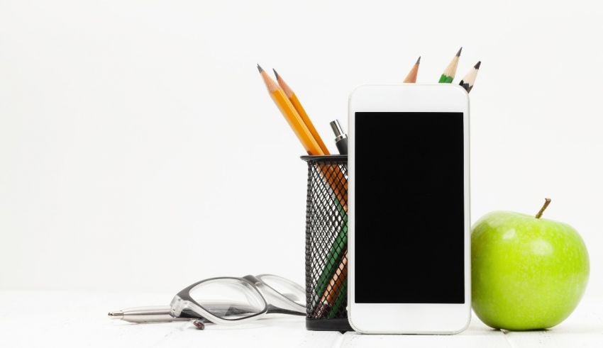 An apple, pencils, glasses and a phone on a white background.