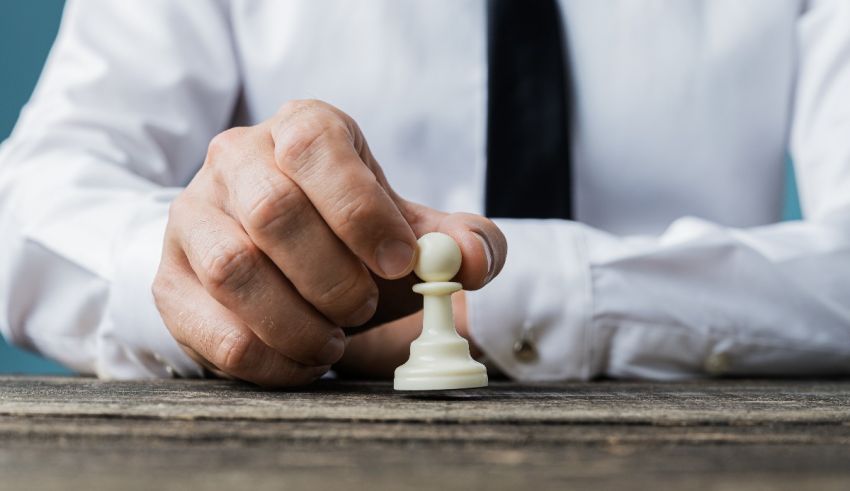 A businessman holding a chess piece on a table.