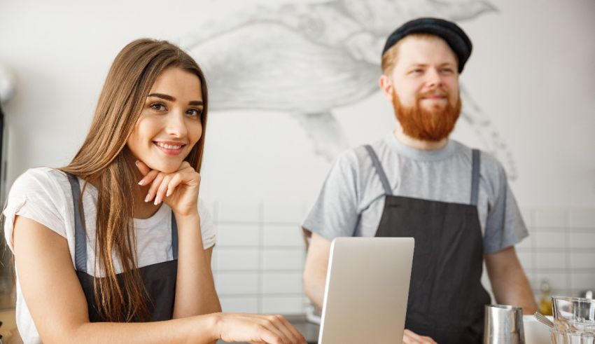 A woman and a man sitting in front of a laptop in a cafe.