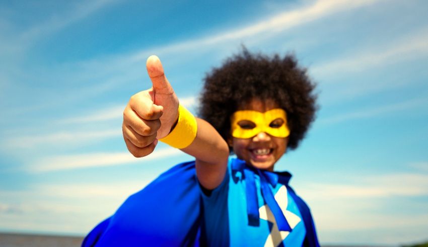 A young boy in a blue superhero costume giving a thumbs up.