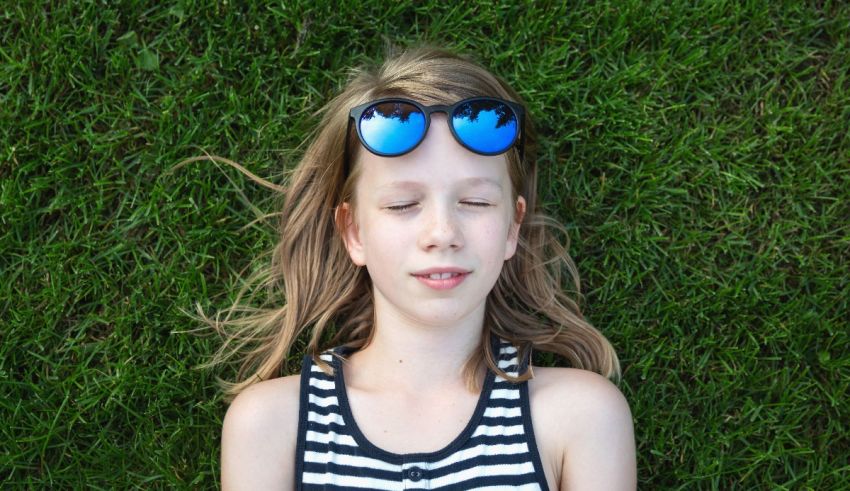 A young girl laying on the grass with sunglasses on.