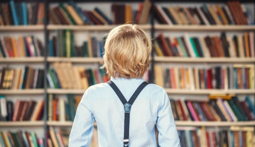 A boy in suspends is standing in front of a book shelf.