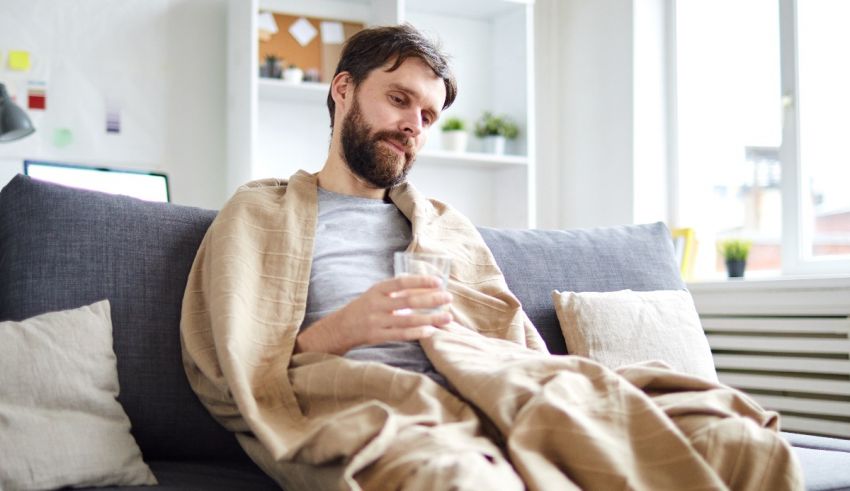 A man sitting on a couch with a blanket wrapped around him.