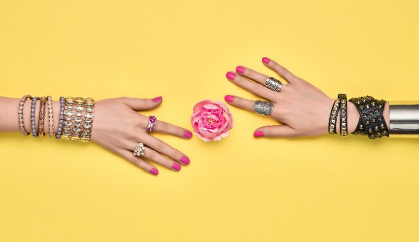 Two women's hands with bracelets and a flower on a yellow background.