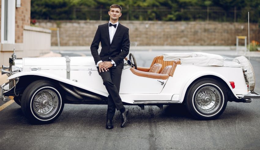 A man in a tuxedo posing next to a classic car.