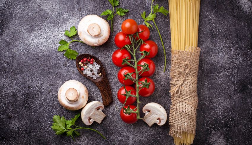 Spaghetti, tomatoes, mushrooms and herbs on a dark background.