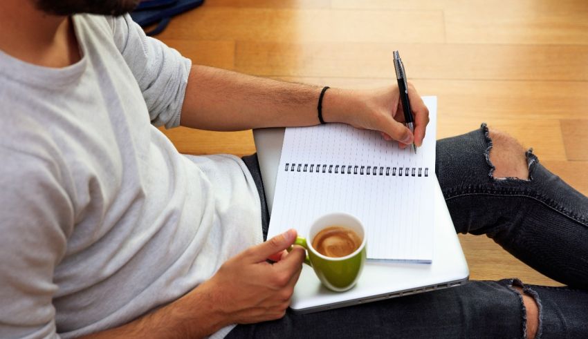 A man writing in a notebook with a cup of coffee.
