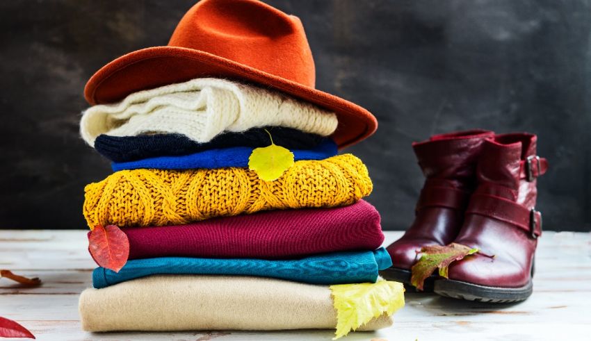 A stack of sweaters, hats and boots on a wooden table.
