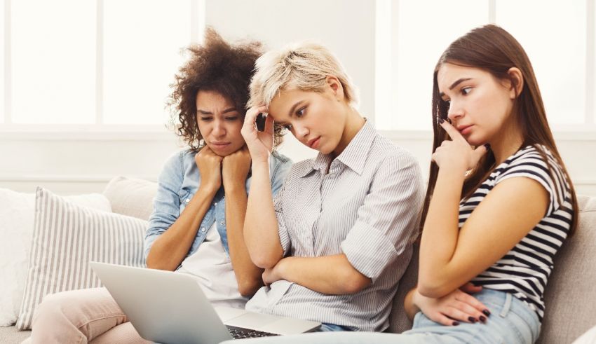 Three women sitting on a couch looking at a laptop.