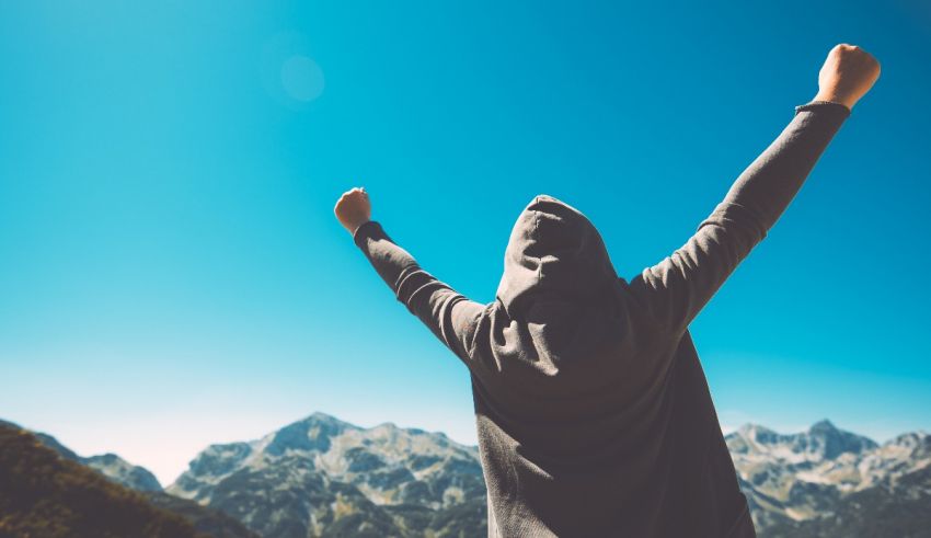 A woman in a hoodie standing on top of a mountain with her arms raised.
