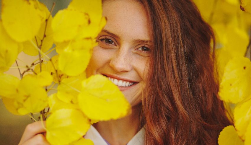 A young woman smiling in front of yellow leaves.