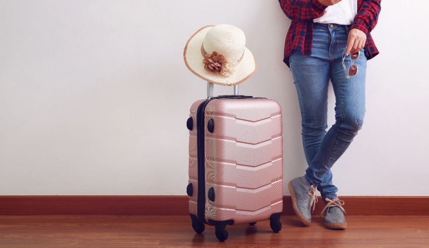 A woman in jeans and a hat standing next to a pink suitcase.