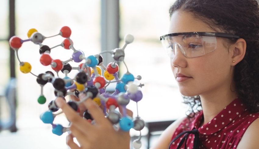 A girl wearing goggles is looking at a model of a molecule.