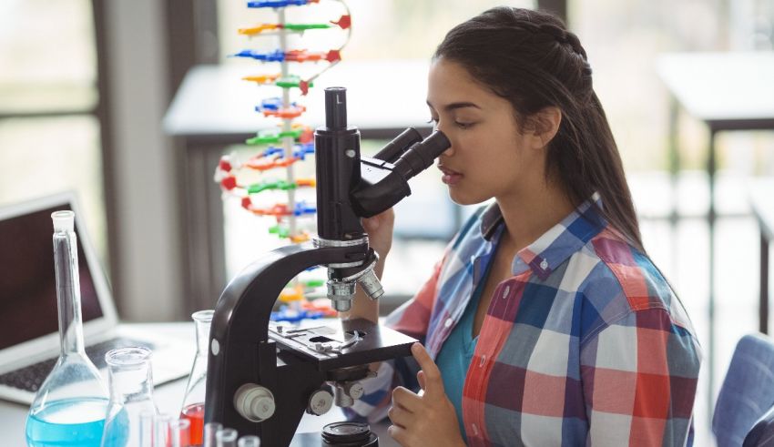 A girl is looking through a microscope in a lab.