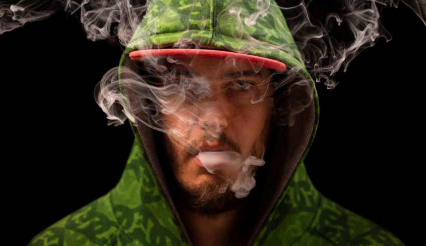 A man in a green hoodie smoking a cigarette.