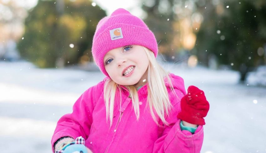 A little girl wearing a pink hat and mittens in the snow.