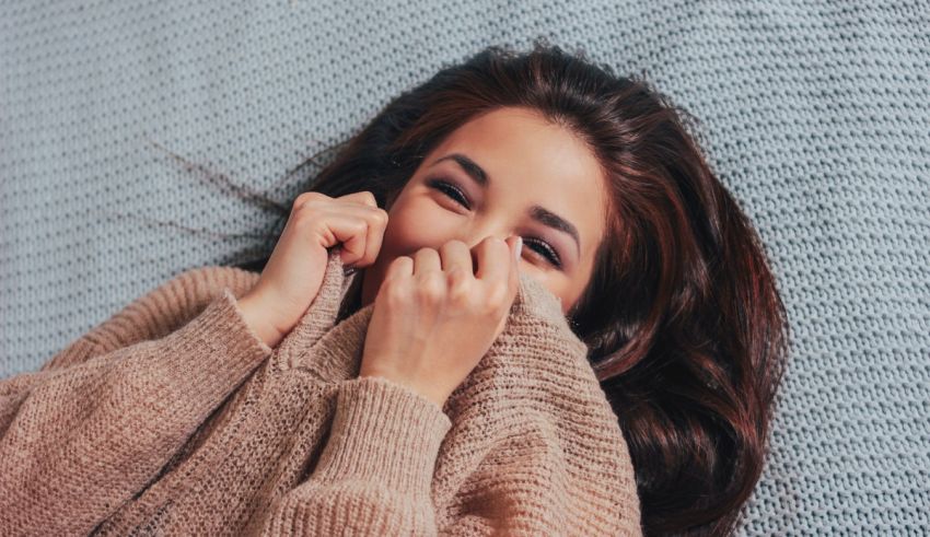 A woman laying on a bed with her face covered in a sweater.