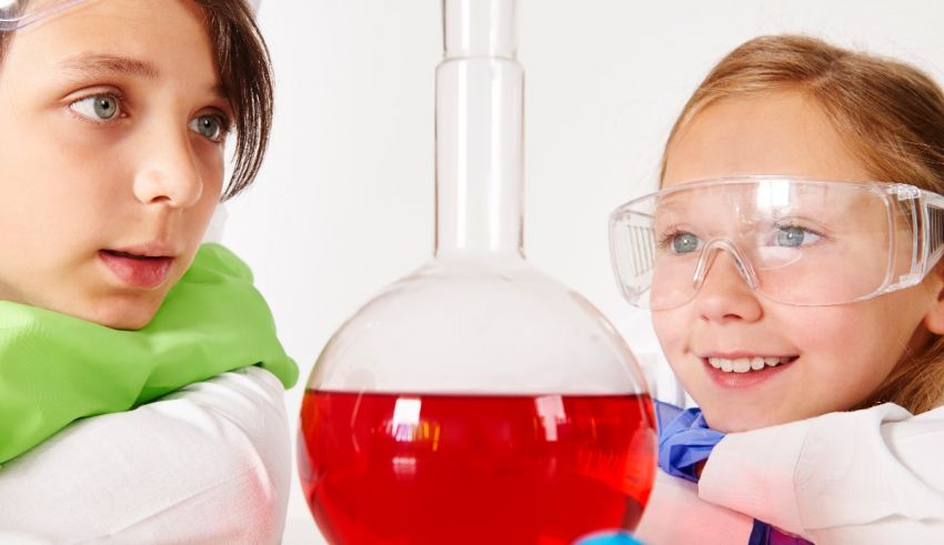 Two girls in lab coats looking at a beaker full of red liquid.