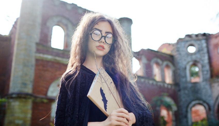 A young woman wearing glasses and holding a book in front of an old castle.