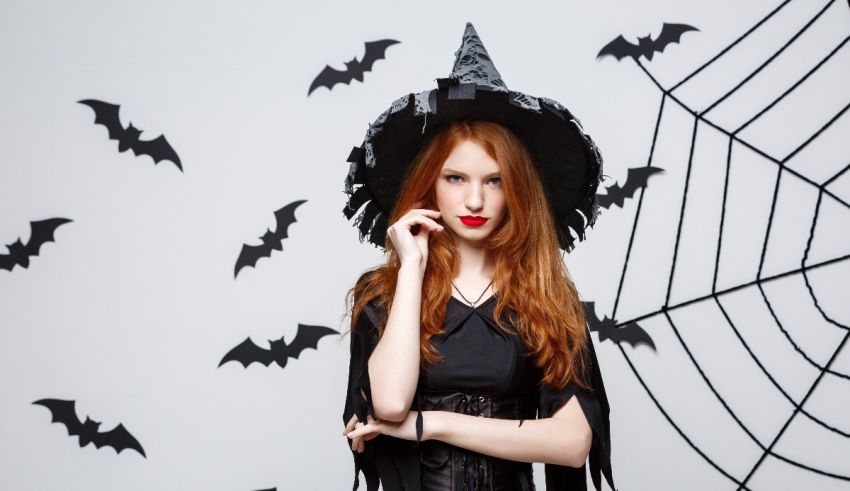 A red haired woman in a witch costume posing in front of a web of bats.