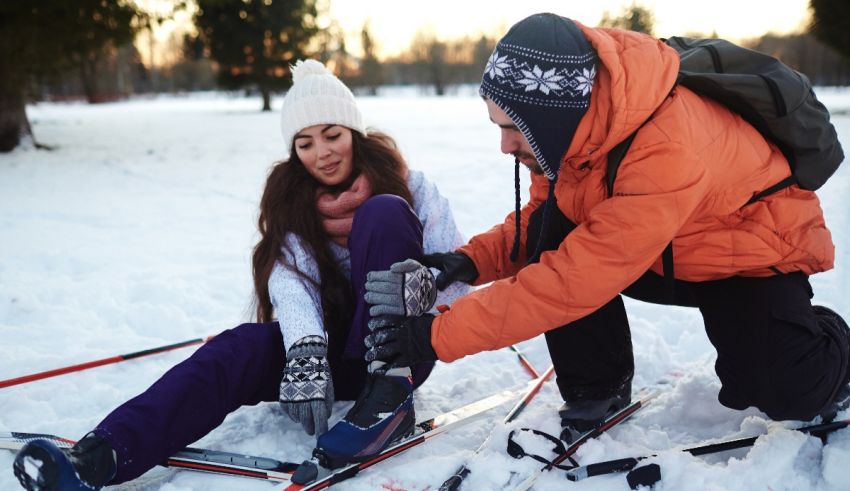 A man and woman tying up their skis in the snow.