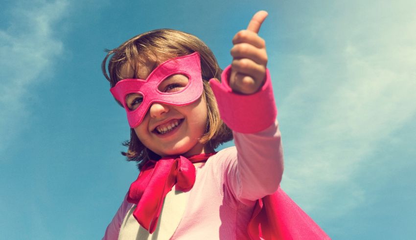 A little girl in a pink superhero costume giving a thumbs up.