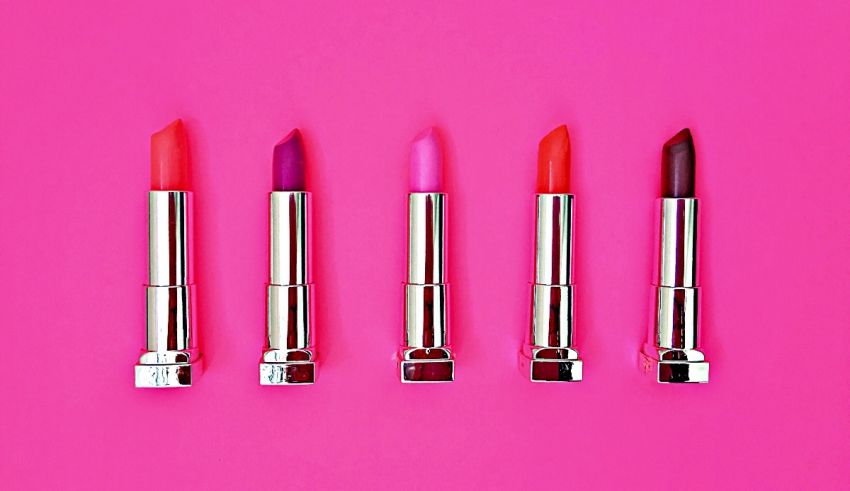 Five lipsticks on a pink background.