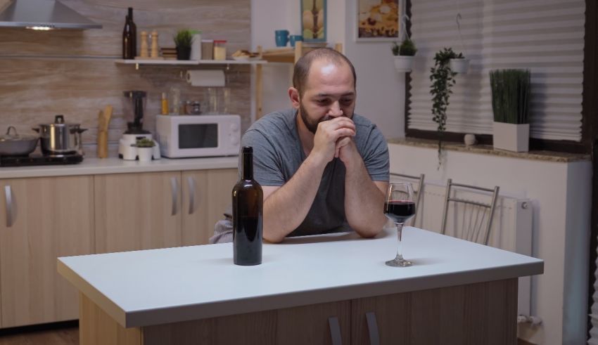 A man sitting at a kitchen table with a glass of wine.