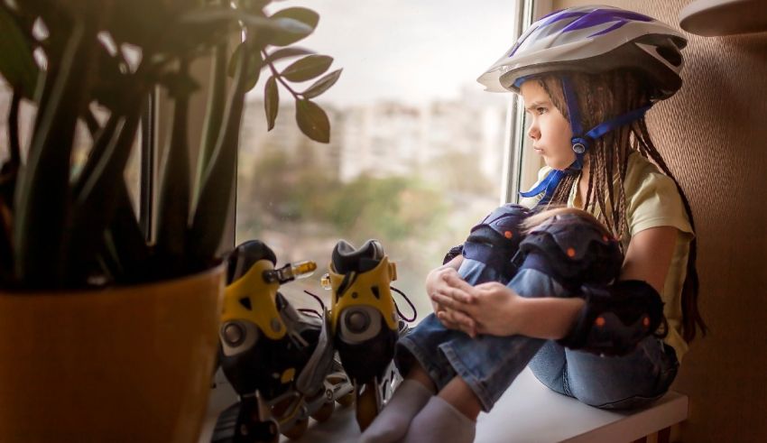 A little girl in a helmet sitting on a window sill.