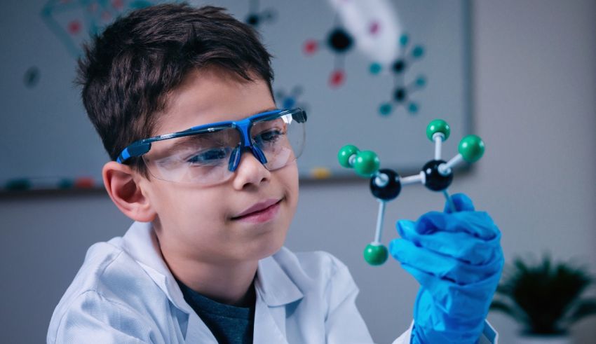 A young boy in a lab coat holding a molecule.