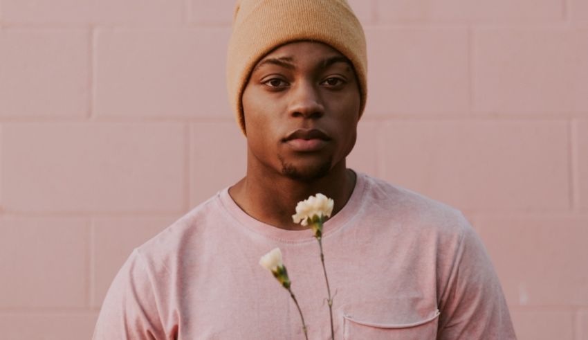 A young man holding a flower in front of a pink wall.