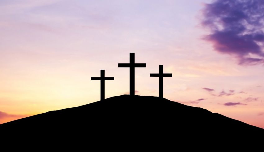 Three crosses on top of a hill at sunset.