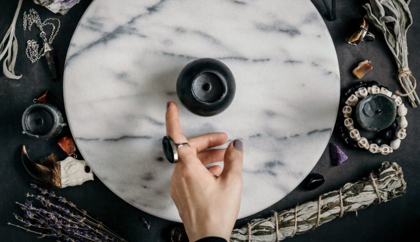 A woman's hand is pointing to a black candle on a marble table.
