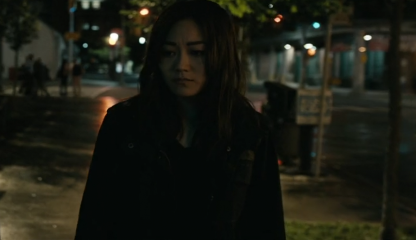 A woman in a black jacket standing on a street at night.