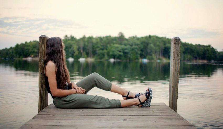 A young woman sitting on a dock near a lake.