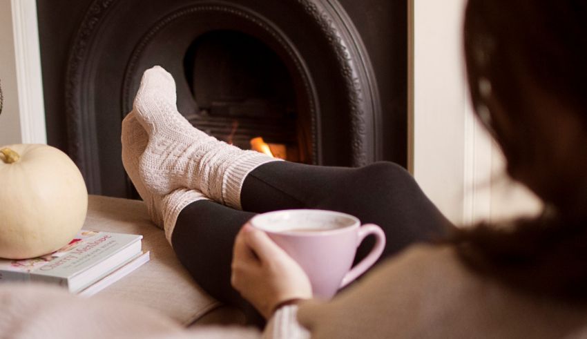 A woman is sitting in front of a fireplace with a cup of coffee.