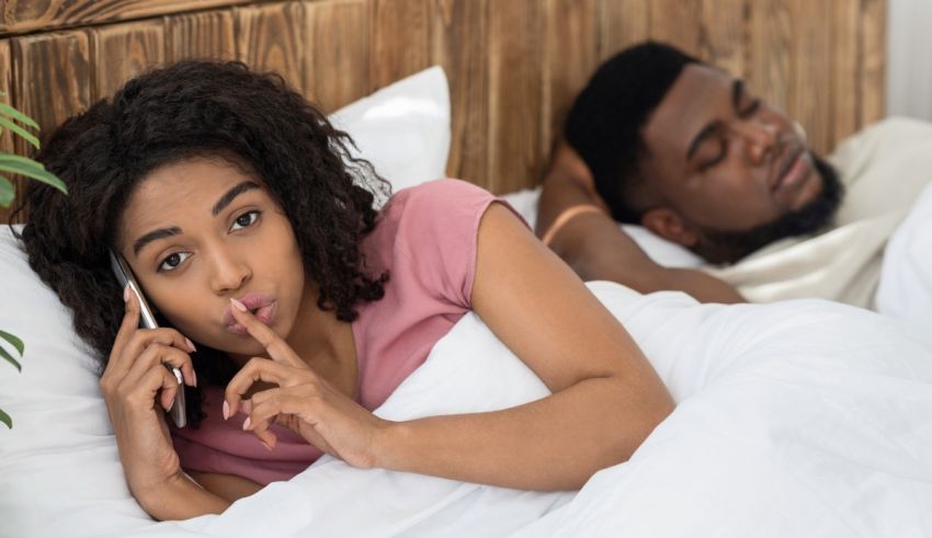 A man and woman laying in bed talking on the phone.