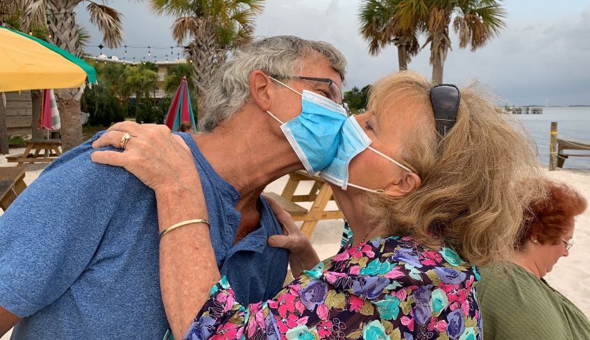 A couple kisses while wearing face masks on the beach.