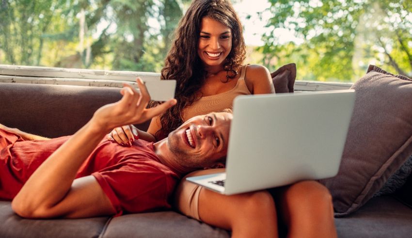 A man and woman sitting on a couch with a laptop and credit card.