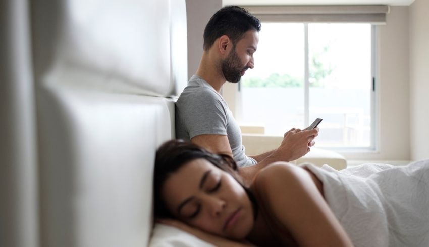 A man and woman sleeping in bed with a cell phone.