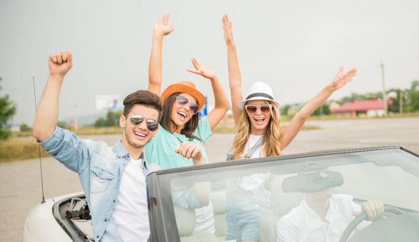 A group of friends in a convertible car waving their hands in the air.