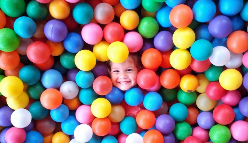 A child peeking out of a ball pit filled with colorful balls.