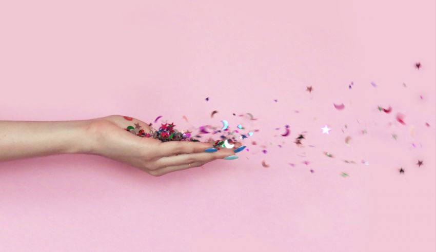 Confetti falling from a woman's hand on a pink background.