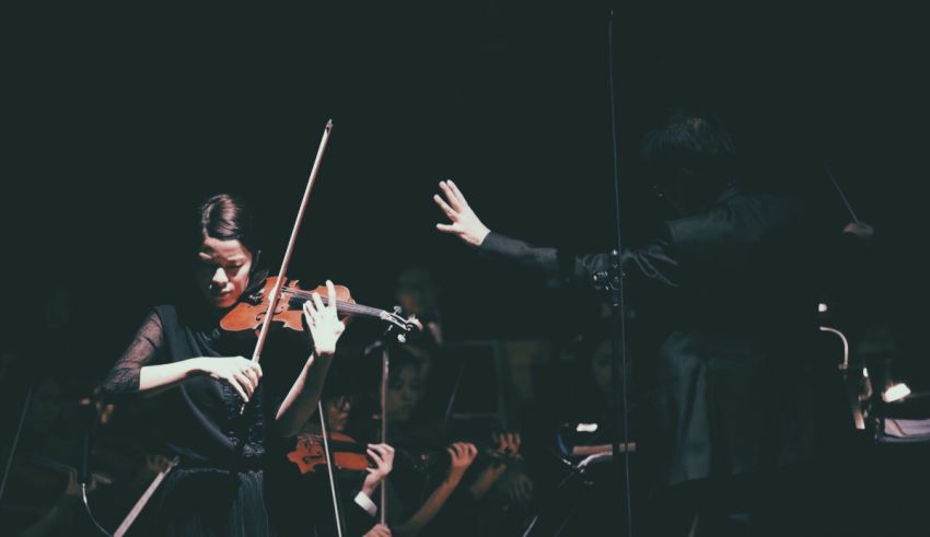 A woman is playing a violin in front of a conductor.