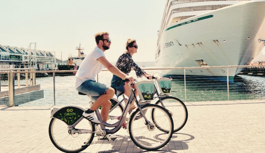 Two people riding bikes in front of a cruise ship.