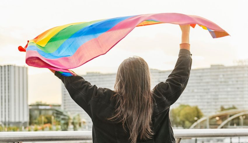 A woman is holding up a rainbow flag in front of a city.