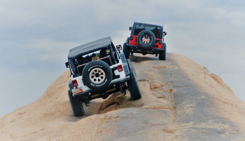 Two jeeps driving up a hill on a cloudy day.