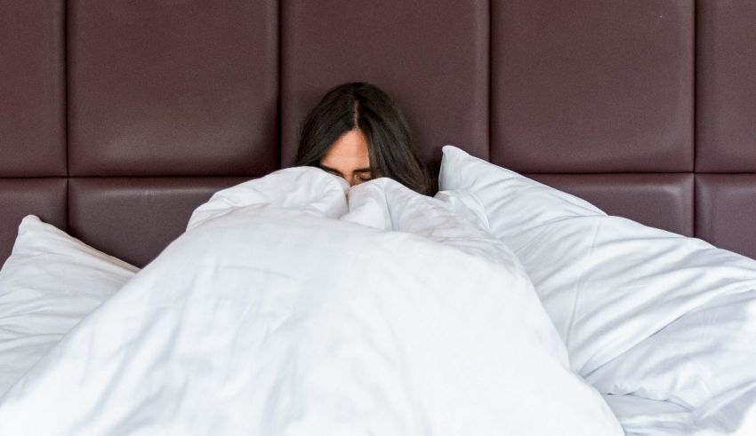 A woman is hiding under a blanket in bed.