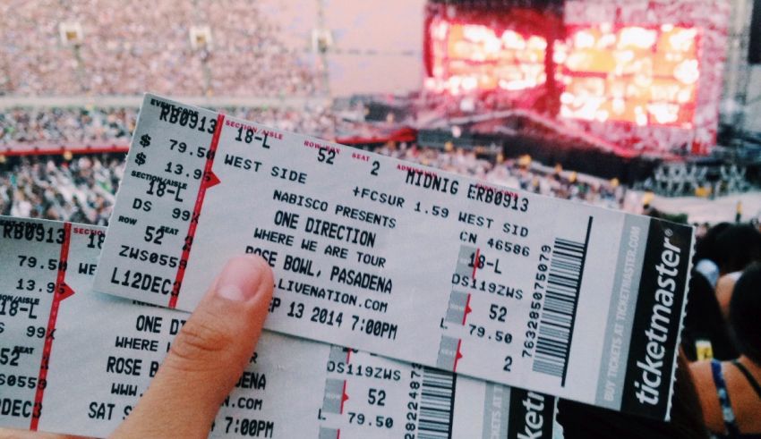 A person holding up two concert tickets in front of a stadium.